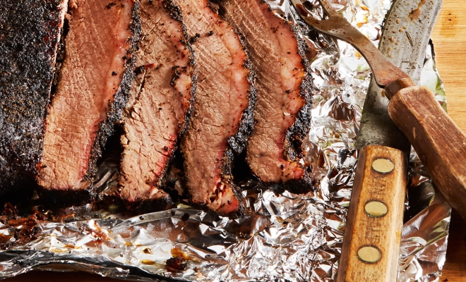 Sliced Brisket on Foil Next to Carving Set