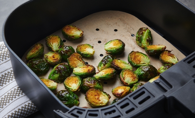 Cooked brussels sprouts lying on an air fryer liner in an air fryer 