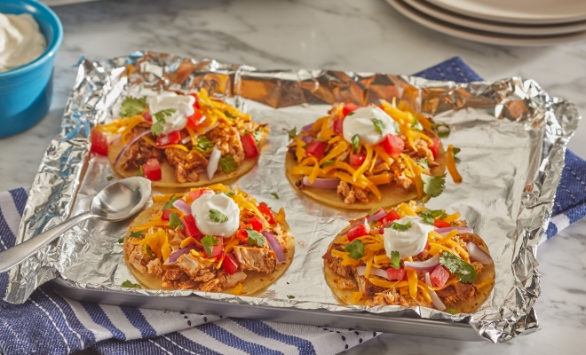 Cheese and chicken tostadas sitting on an aluminum foil lined baking sheet alongside a toaster oven