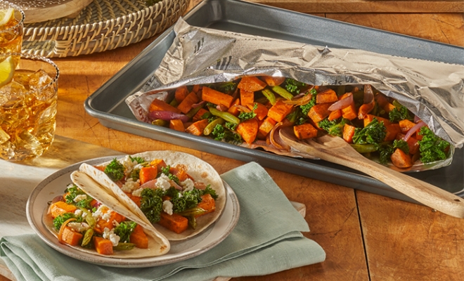 Spiced sweet potato and kale tacos sitting alongside an open aluminum foil grill bag set on top of a wooden table