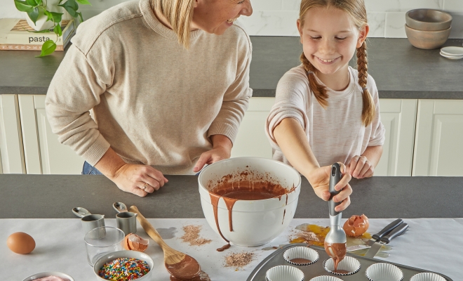 mother and daughter making cupcakes on a kitchen island topped with countertop prep paper