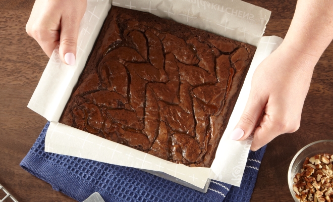 A person pulling baked brownies out of a square pan using a parchment sling