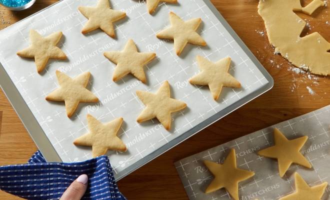 A person holding a parchment lined cookie sheet with star shaped sugar cookies