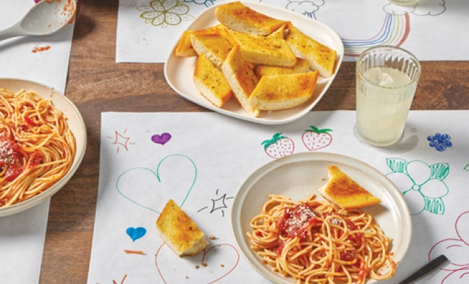 placemats made out of countertop prep paper sitting at a dinning table and topped with plates of spaghetti