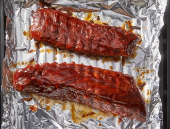 Two slabs of ribs sitting on a piece of aluminum foil on the grill