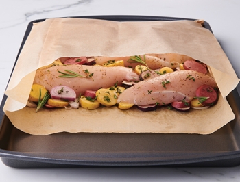 Chicken and vegetable in an open parchment cooking bag sitting on a baking sheet