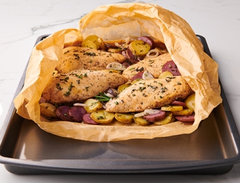 Cooked chicken and vegetable in an open parchment cooking bag sitting on a baking sheet