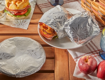 Sandwiches wrapped in Reynolds Wrap Fun foil on an outdoor table alongside a picnic basket