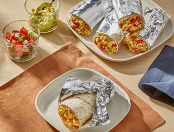 Breakfast burritos wrapped in foil stacked on a plate
