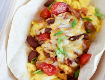 scrambled egg burrito topped with beans, rice and tomatoes