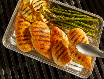 Grilled chicken breasts, asparagus and squash in a grill pan on top of a grill grate