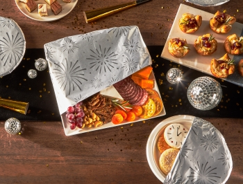 NYE themed buffet table with platters of food partially covered in foil