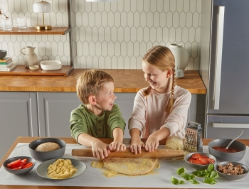 two kids rolling pizza dough on a kitchen counter topped with Reynolds Kitchens Countertop Prep Paper