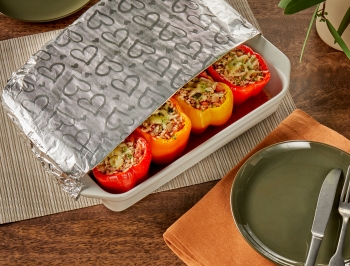 stuffed peppers sitting in a white ceramic dish and partially covered in Reynolds Wrap Fun Foil with embossed heart pattern