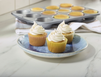 vanilla cupcakes with white frosting in baking cups sitting on a plate