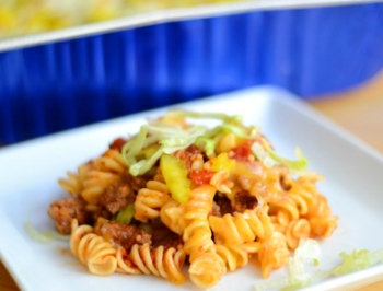 serving of cheeseburger casserole on a white plate with a reynolds kitchens disposable pan in the background