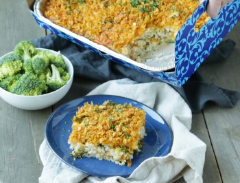 chicken broccoli and rice casserole in a disposable pan sitting on table alongside a plate 