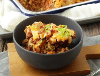 hamburger casserole sitting in a black bowl on a wood cutting board