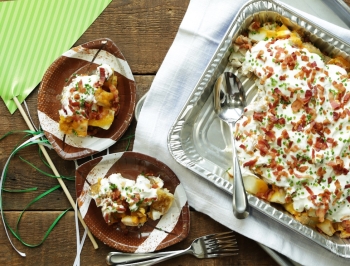 loaded baked potato casserole in a disposable aluminum container sitting on a wood table