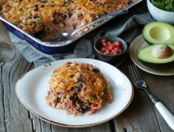 southwest chicken casserole in a disposable pan sitting on a rustic wood table with one scoop removed and sitting on a plate