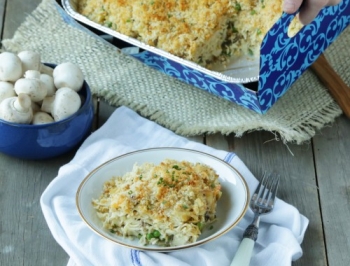 disposable pan filled with tuna fish casserole sitting on a wood table with a serving dished up on a while plate