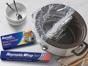 slow cooker with an aluminum foil divider and one side of the bowl lined with a slow cooker liner sitting alongside a package of Reynolds Kitchens Slow Cooker Liners and Reynolds Wrap Heavy Duty Foil