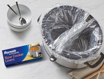 slow cooker with an aluminum foil divider and both sides of the bowl lined with a slow cooker liner sitting alongside a package of Reynolds Kitchens Slow Cooker Liners and Reynolds Wrap Heavy Duty Foil