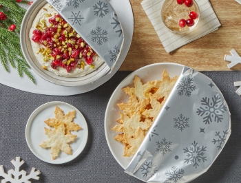 snowflakes shaped pita chips and whipped goat cheese spread partially covered in Reynolds Wrap Fun Foil with Snowflakes Pattern sitting on a kitchen table with festive decor
