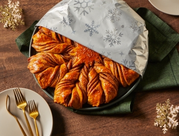 snowflake shaped money bread partially covered with Reynolds Wrap Fun Foil with Snowflakes Pattern sitting on a table alongside plates and forks