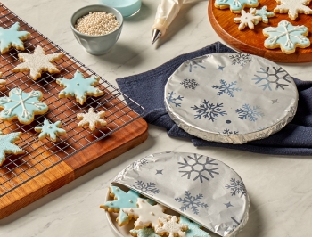 snowflake shaped sugar cookies decorated in blue and white frosting sitting on a kitchen counter partially covered in Reynolds Wrap Fun Foil with Snowflakes Pattern