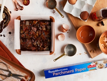The brownie batter shown in a parchment lined 8x8 pan and a box of Reynolds Kitchens parchment paper nearby