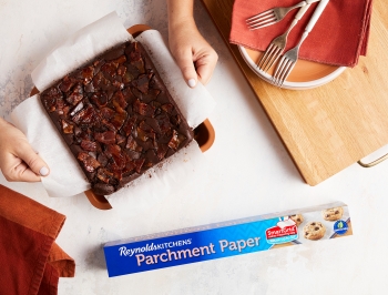 A person grabbing the parchment paper lining to pull out the finished brownies to make it easier to cut them