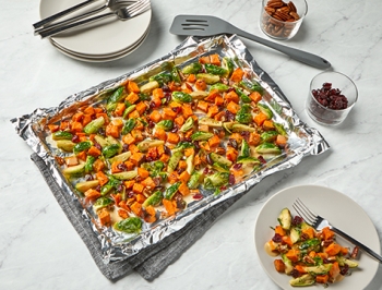 Roasted Sweet Potatoes and Brussels Sprouts with Cranberries and Pecans on a foil lined baking sheet