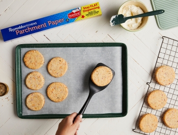 Baked cookies being easily removed from non stick parchment paper on a sheet pan and being placed on a wire cooling rack