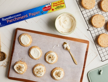 Baked cookies being frosted on a parchment lined baking sheet