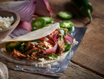 Grilled pulled pork tacos sitting on a piece of aluminum foil surrounded by taco toppings